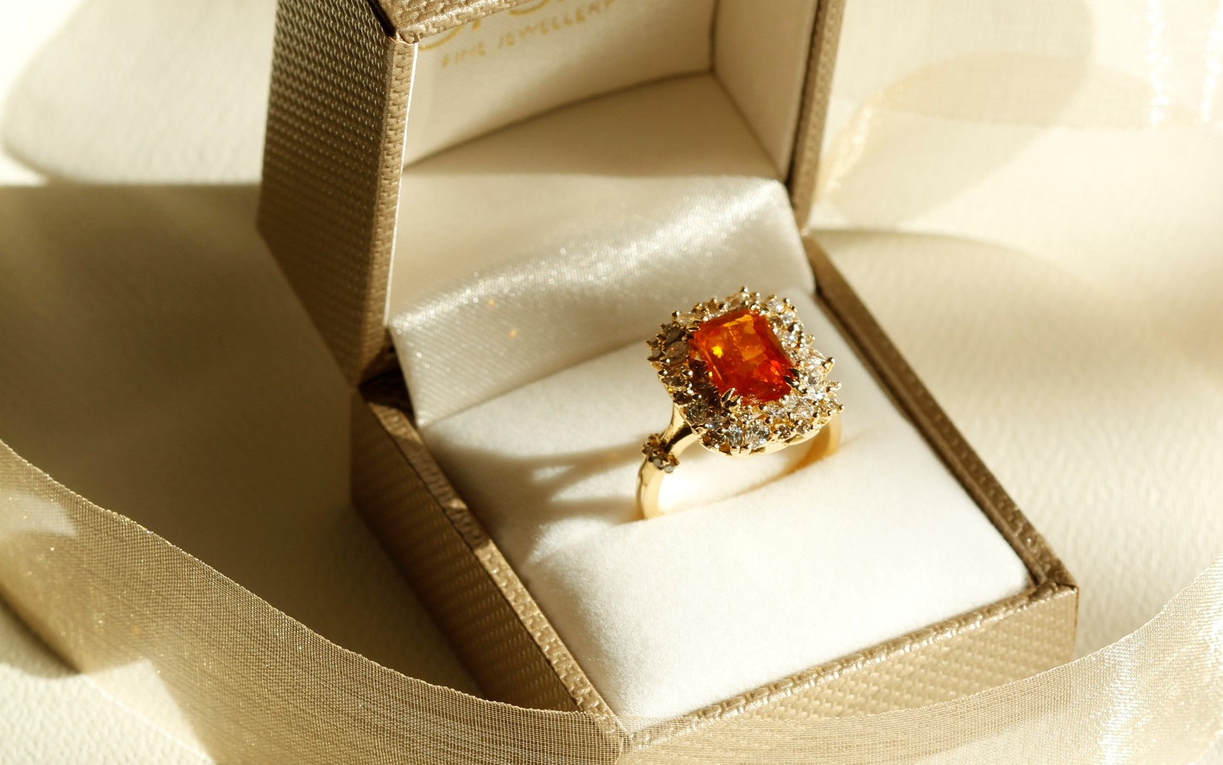 Marquise cut diamond, pear cut diamond, and round brilliant cut diamond surrounding an orange sapphire in a yellow gold ring