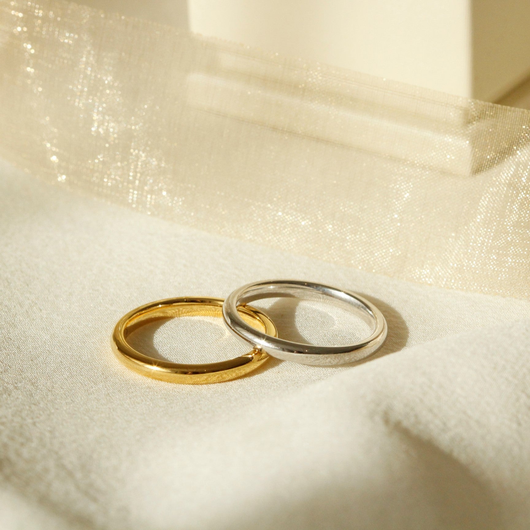 Wedding Rings laying on one another on cloth in the sun, one is yellow gold and the other is white gold