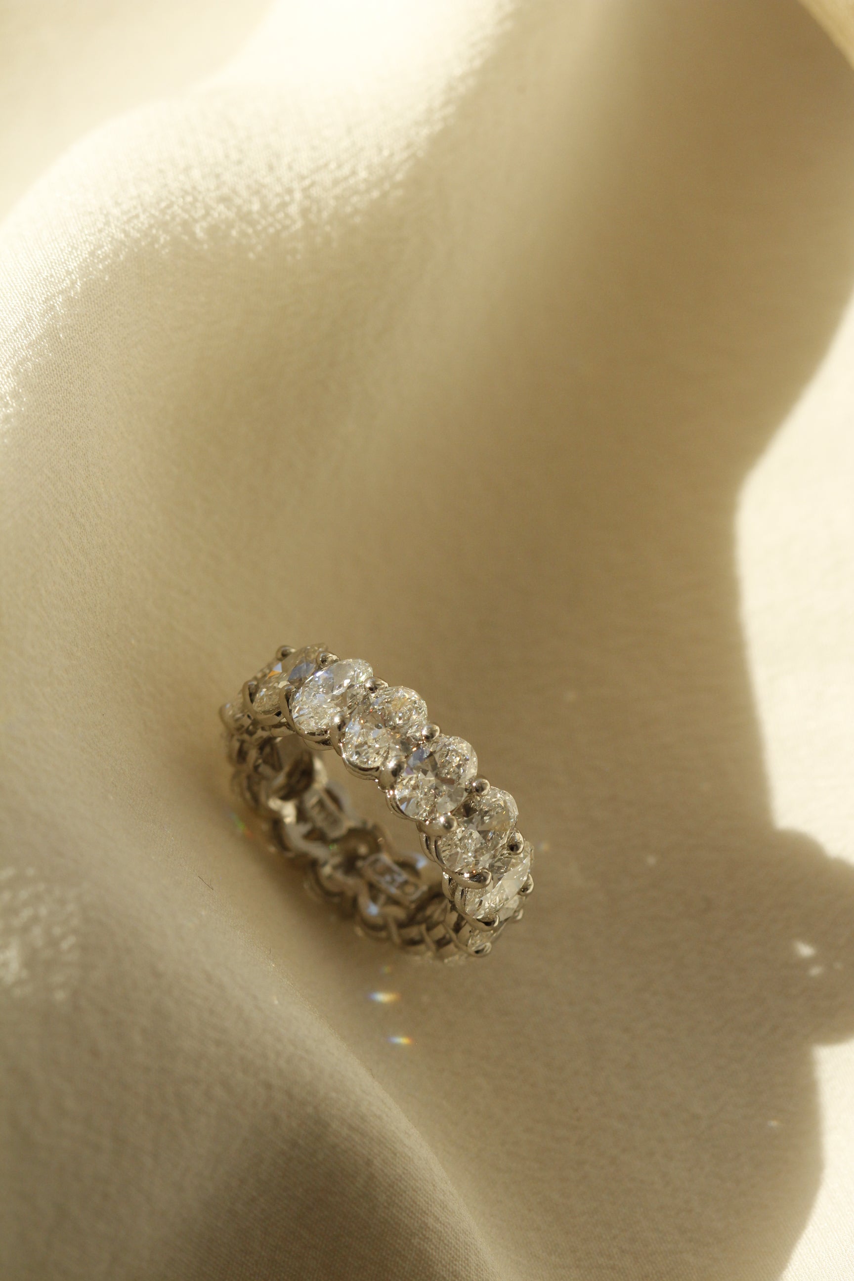 Infinity ring with 11 Oval cut diamonds set in platinum lying on fabric in the sun