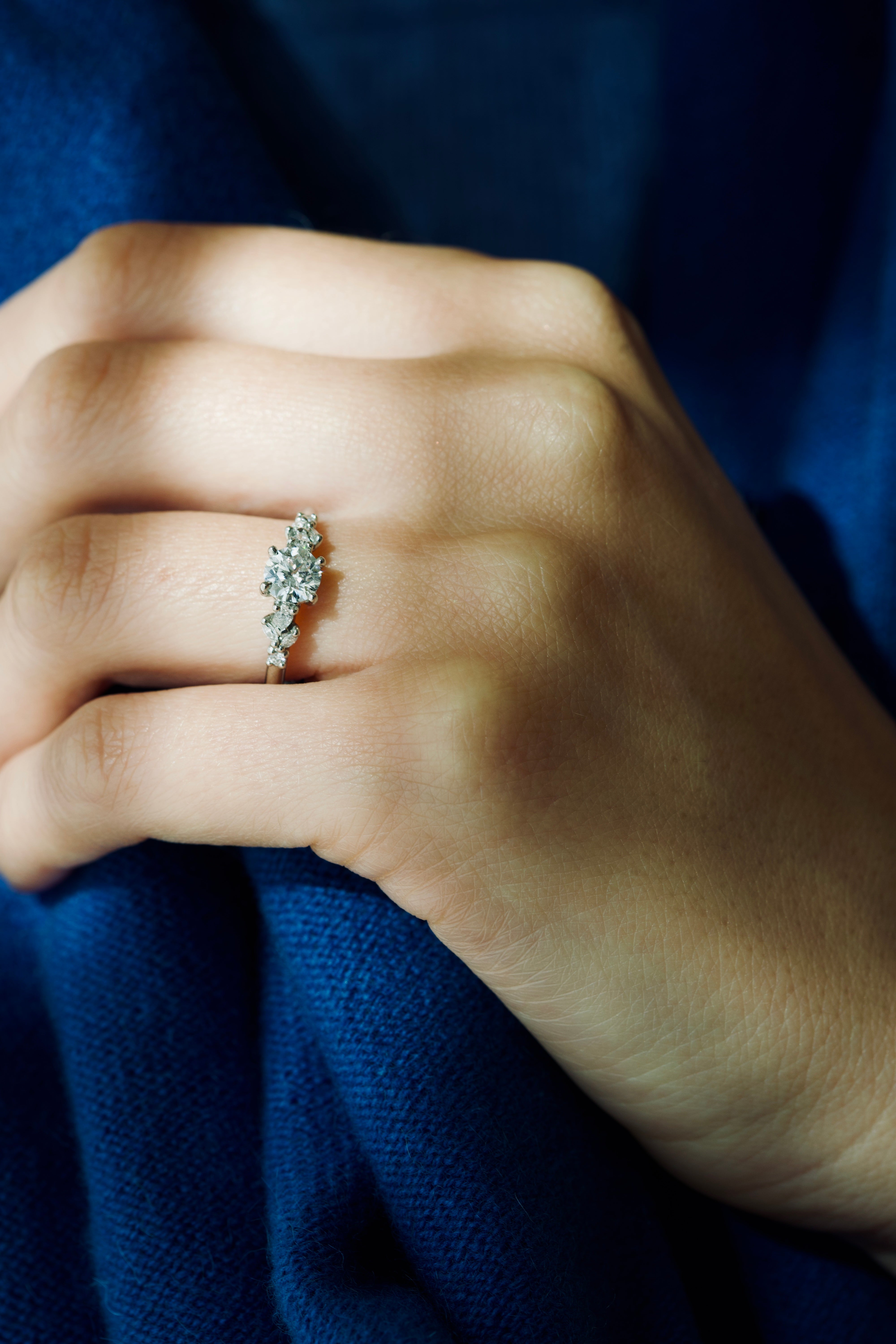 Close-up of a hand wearing a white gold Nesso diamond engagement ring with a blue fabric background | Orsini