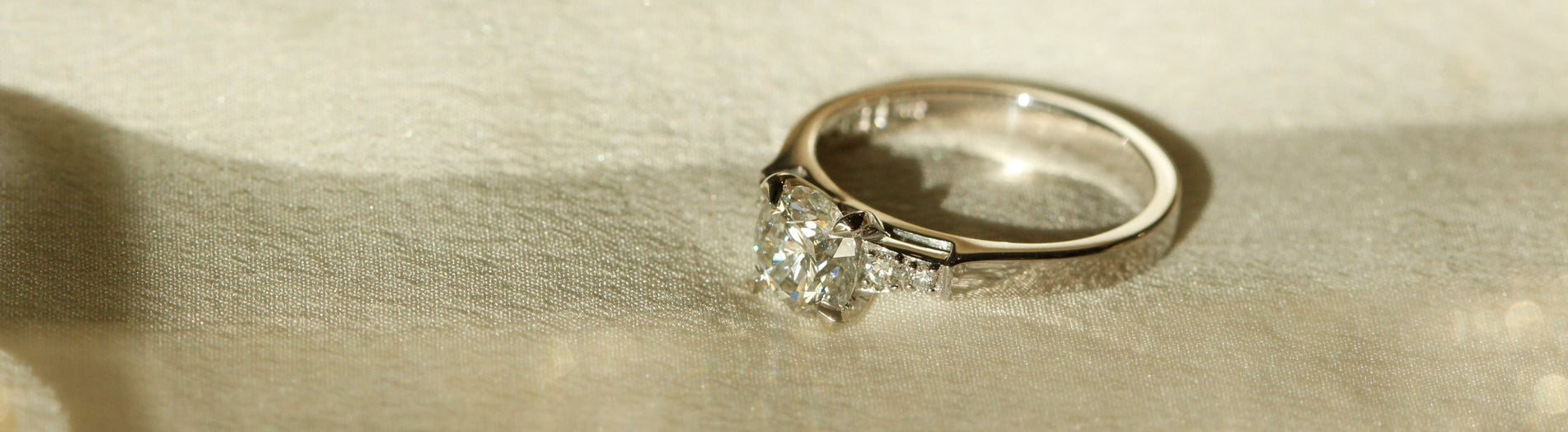 Four Claw Engagement Ring in Platinum Lying on White Fabric Banner