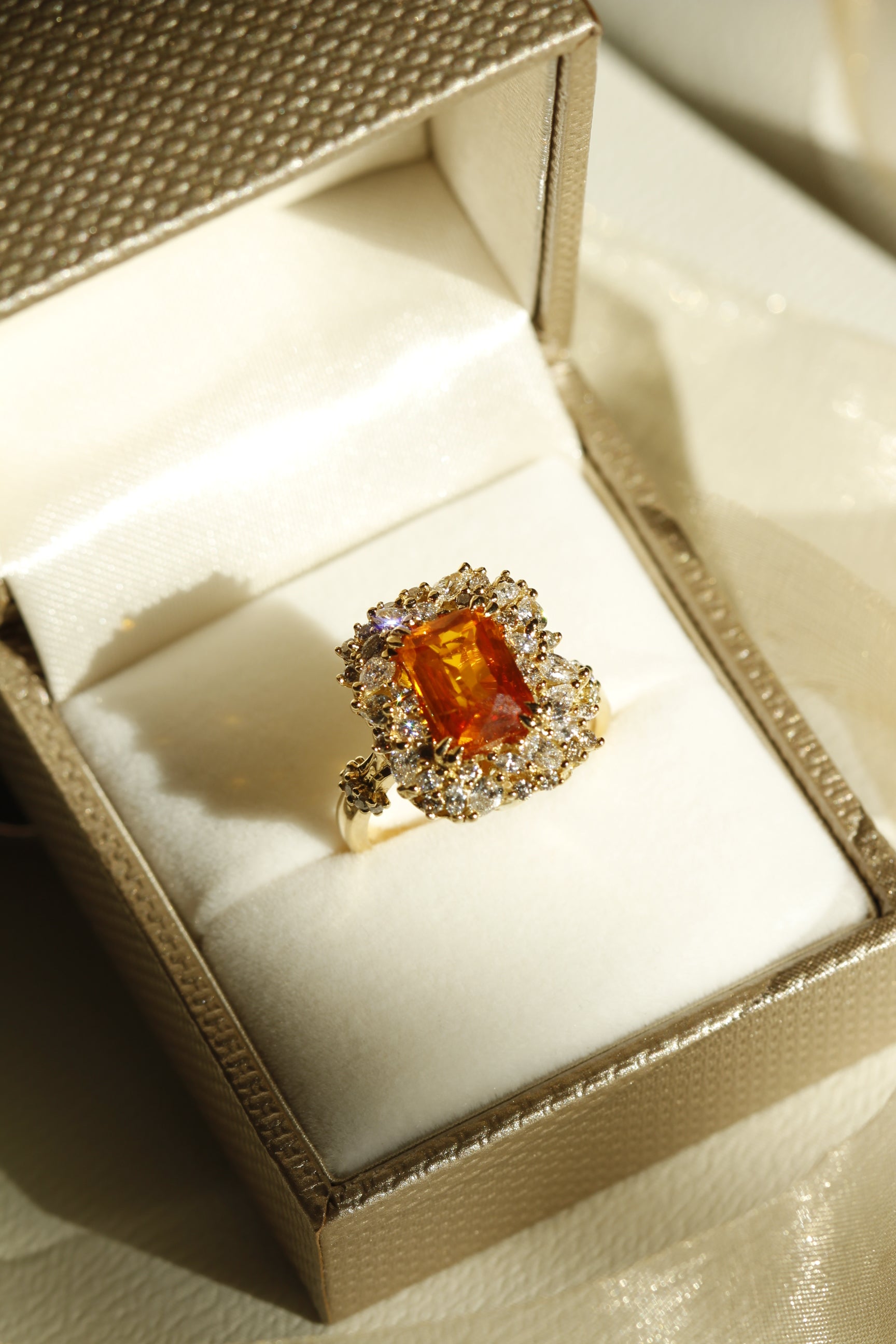 Marquise cut diamond, pear cut diamond, and round brilliant cut diamond surrounding an orange sapphire in a yellow gold ring for mobile