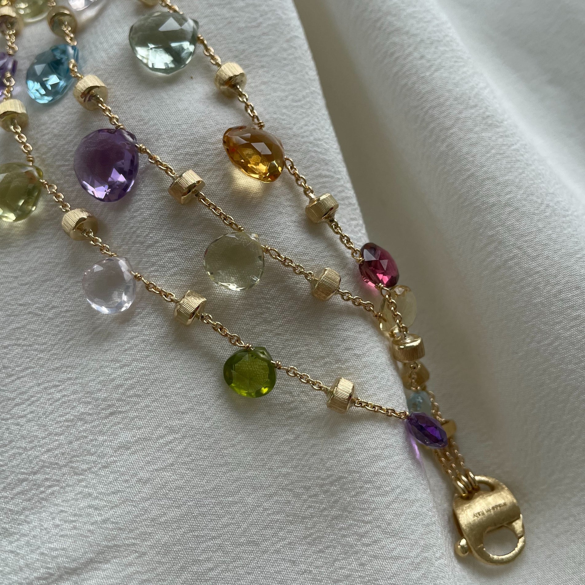 Yellow gold and mixed gemstones three strand bracelet Paradise collection by Marco Bicego image taken on white cloth 