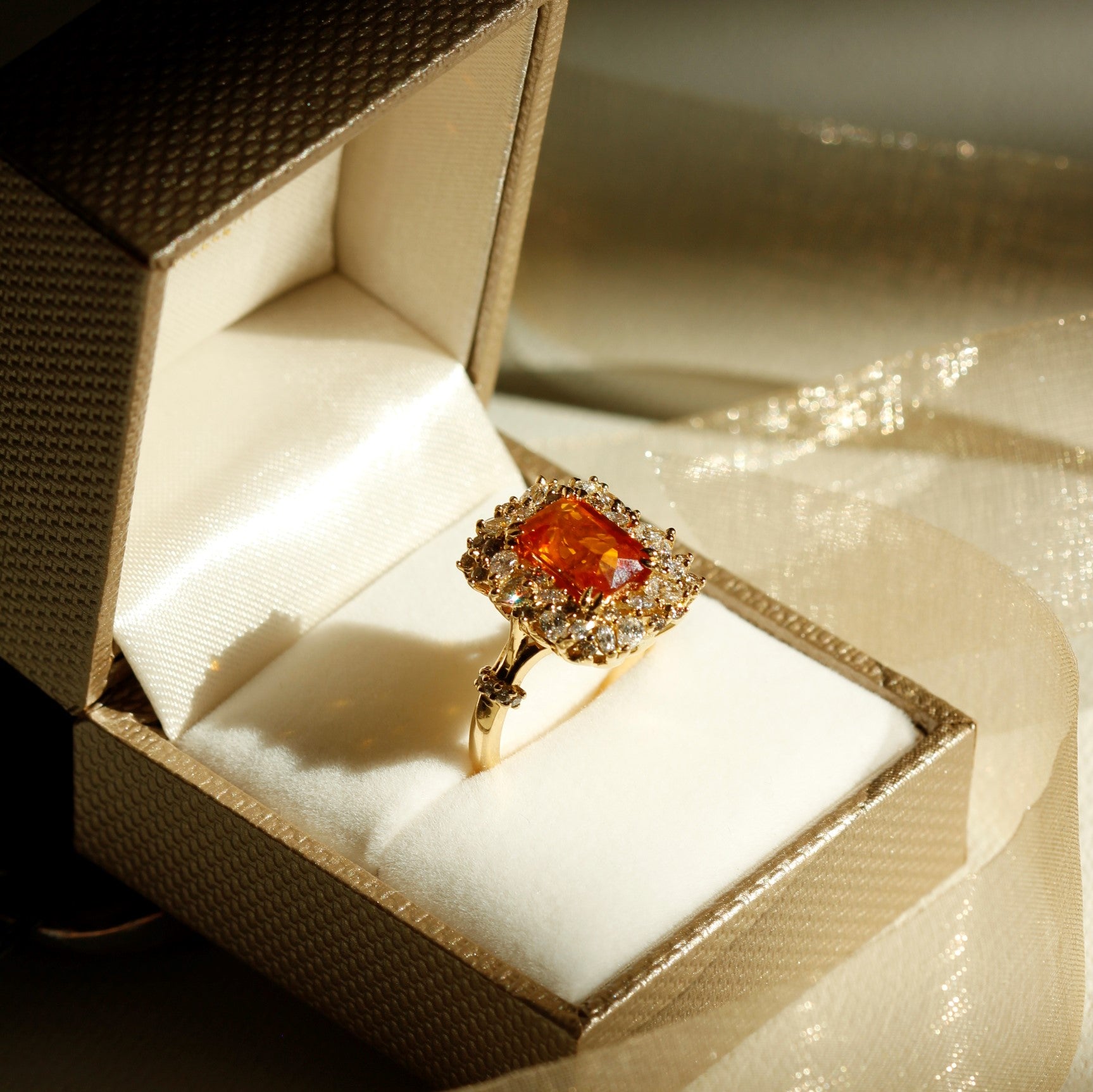 Orange sapphire surrounded by white and champagne diamonds set in 18k yellow gold ring taken in gold ring box copped for square for Orisni Fine Jewellery homepage image 